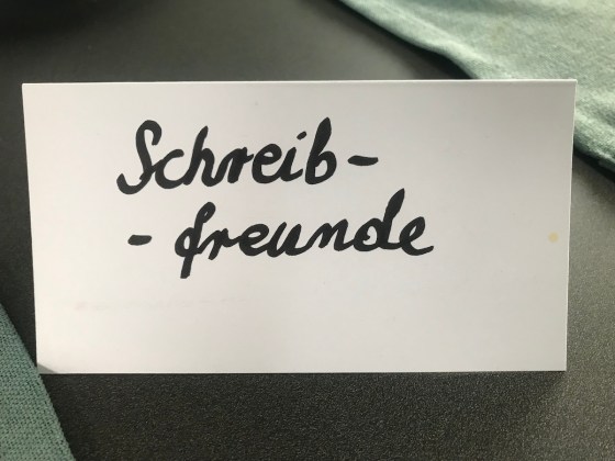 Weißer, zu einem "Aufsteller" gefalteter Karton mit dem handschriftlichen Text "Schreibfreunde"
